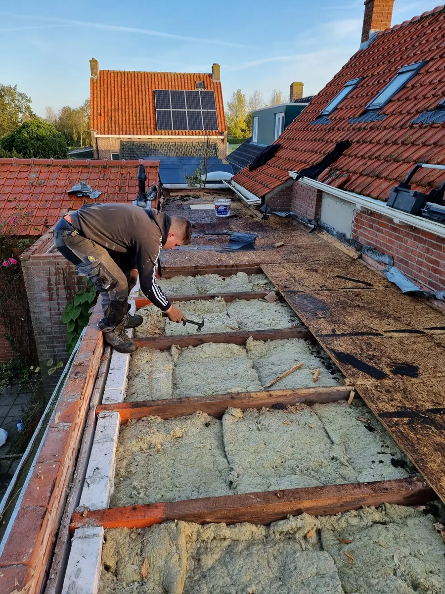 Een vakman legt isolatie tussen de sporen van een open dak.