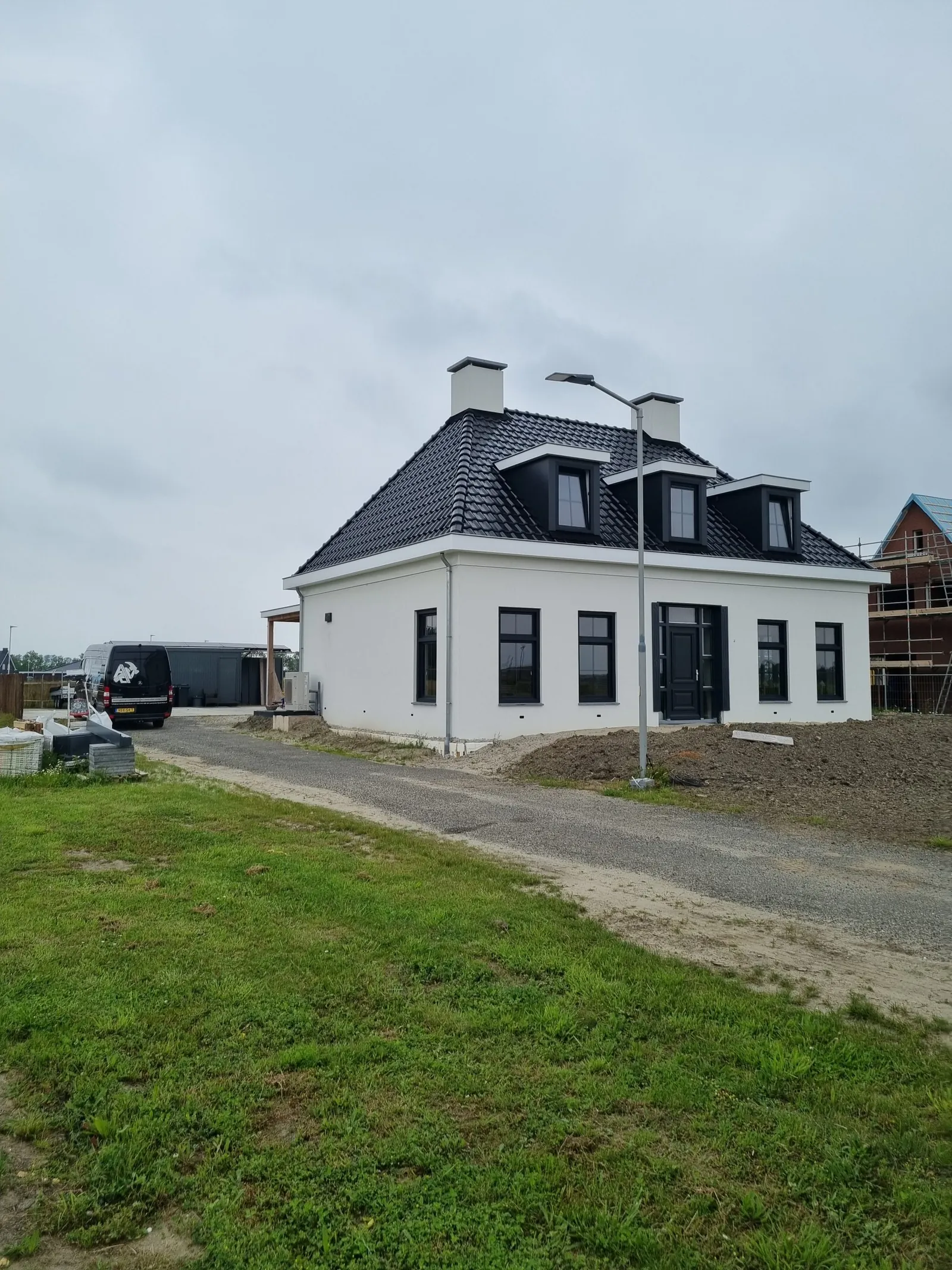 Een witte vrijstaande woning met donker pannendak en drie dakkapellen.